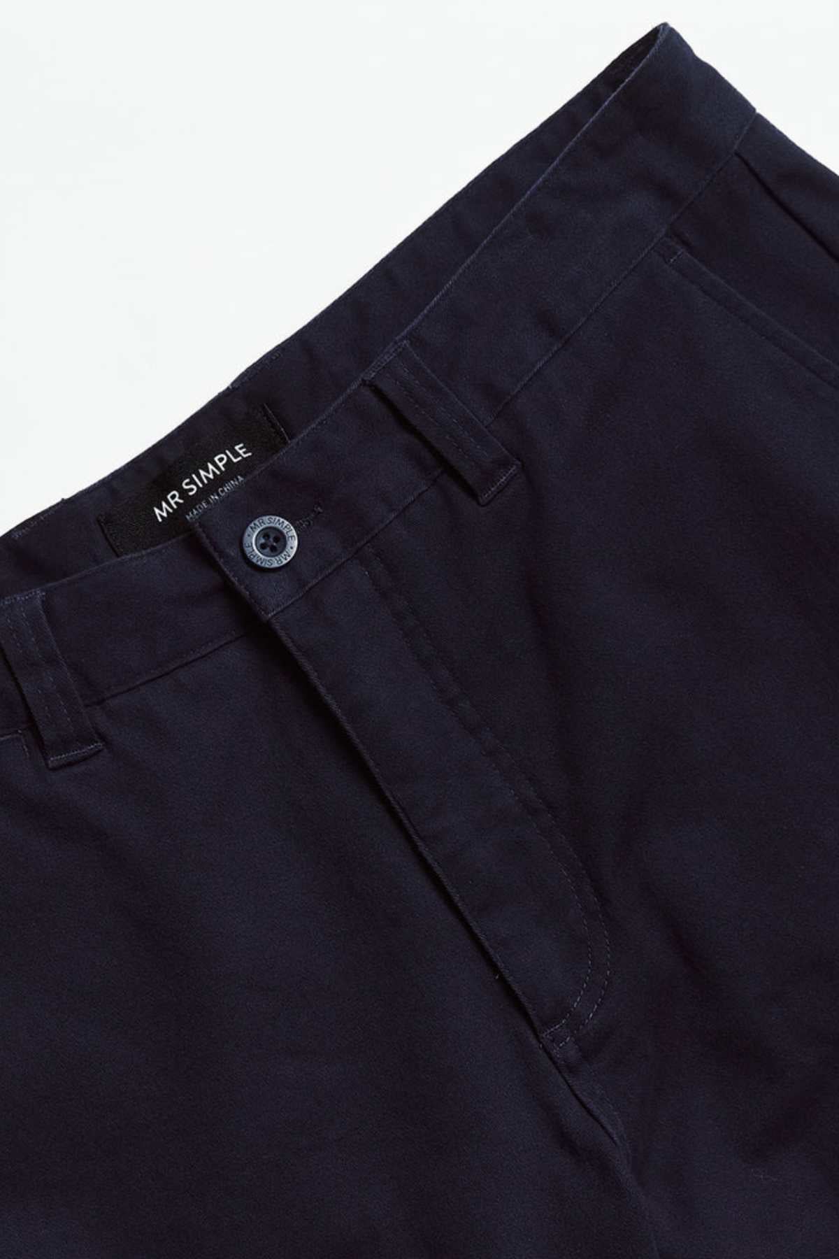 Close-up of Mr Simple Wilson Standard Chino in dark blue organic cotton, featuring a single button and zip fly. The label "Mr Simple" is visible on the inner waistband. These relaxed-fit trousers are displayed against a plain white background.