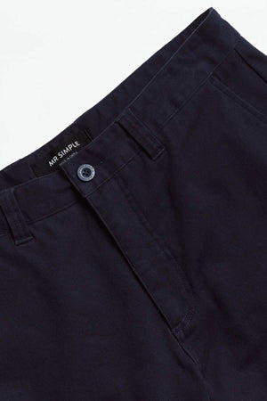 Close-up of Mr Simple Wilson Standard Chino in dark blue organic cotton, featuring a single button and zip fly. The label "Mr Simple" is visible on the inner waistband. These relaxed-fit trousers are displayed against a plain white background.