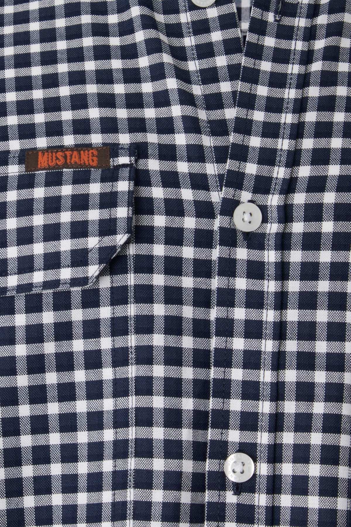 Close-up image of the Mustang Signature Check Shirt for men, crafted from high-quality cotton and featuring a black and white checkered pattern with a pocket on the left side. The word "MUSTANG" is embroidered in red on the pocket, showcasing Mustang's signature style. The shirt also has white buttons down the front.