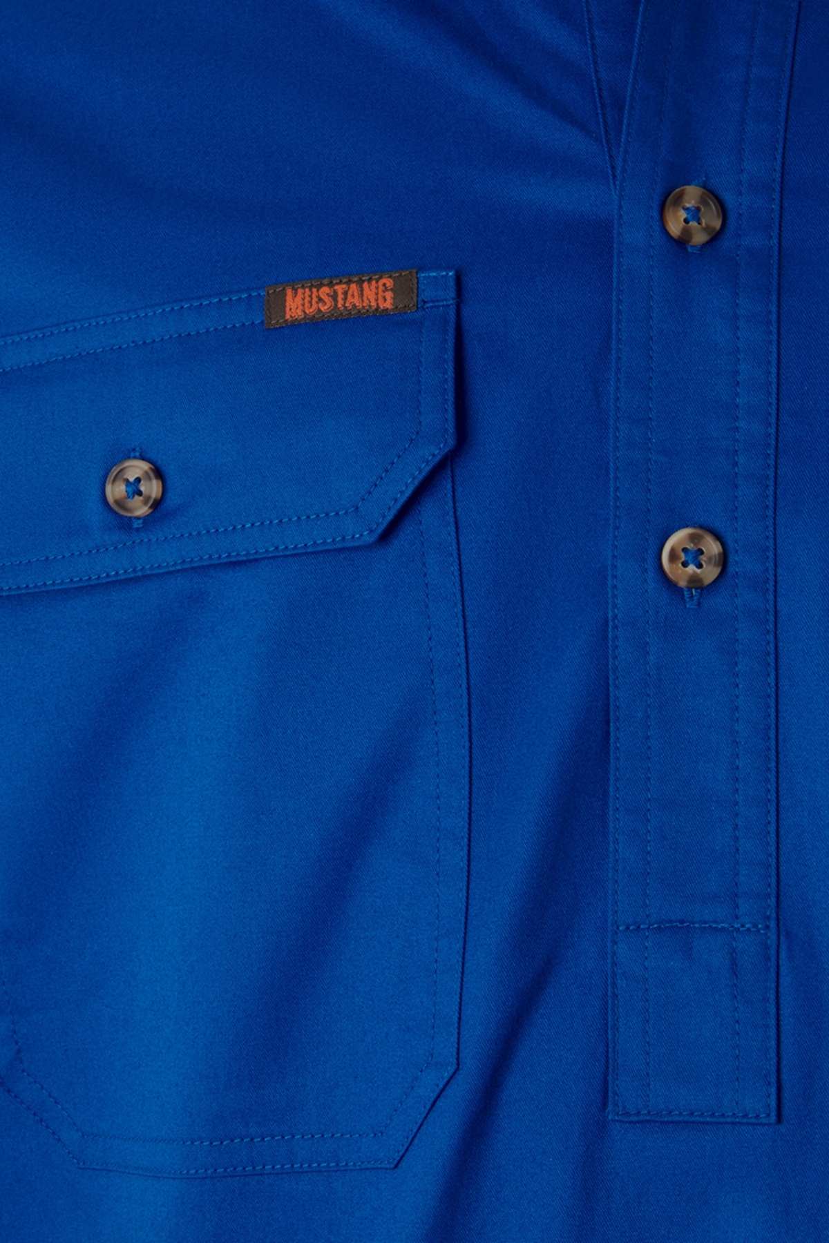 Close-up of the Mustang Signature Closed Front Workshirt in blue, featuring brown buttons, a front pocket, and an orange "MUSTANG" tag above the pocket that highlights its quality cotton fabric.