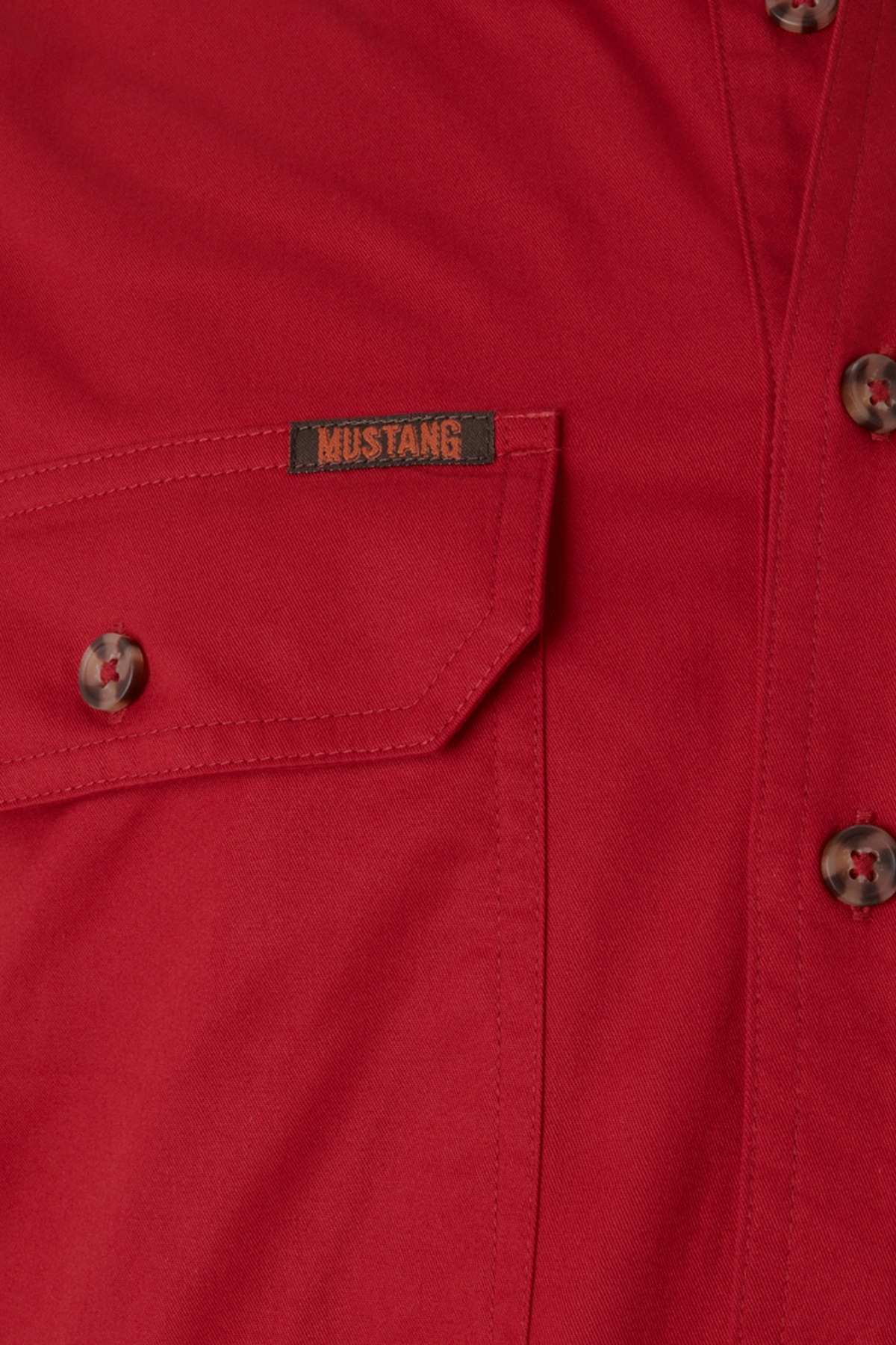 A detailed view of the Mustang Signature Closed Front Workshirt in red, featuring a buttoned pocket with a small "Mustang" label. Made from durable cotton, this men's shirt is complete with brown buttons, embodying tough workwear style.