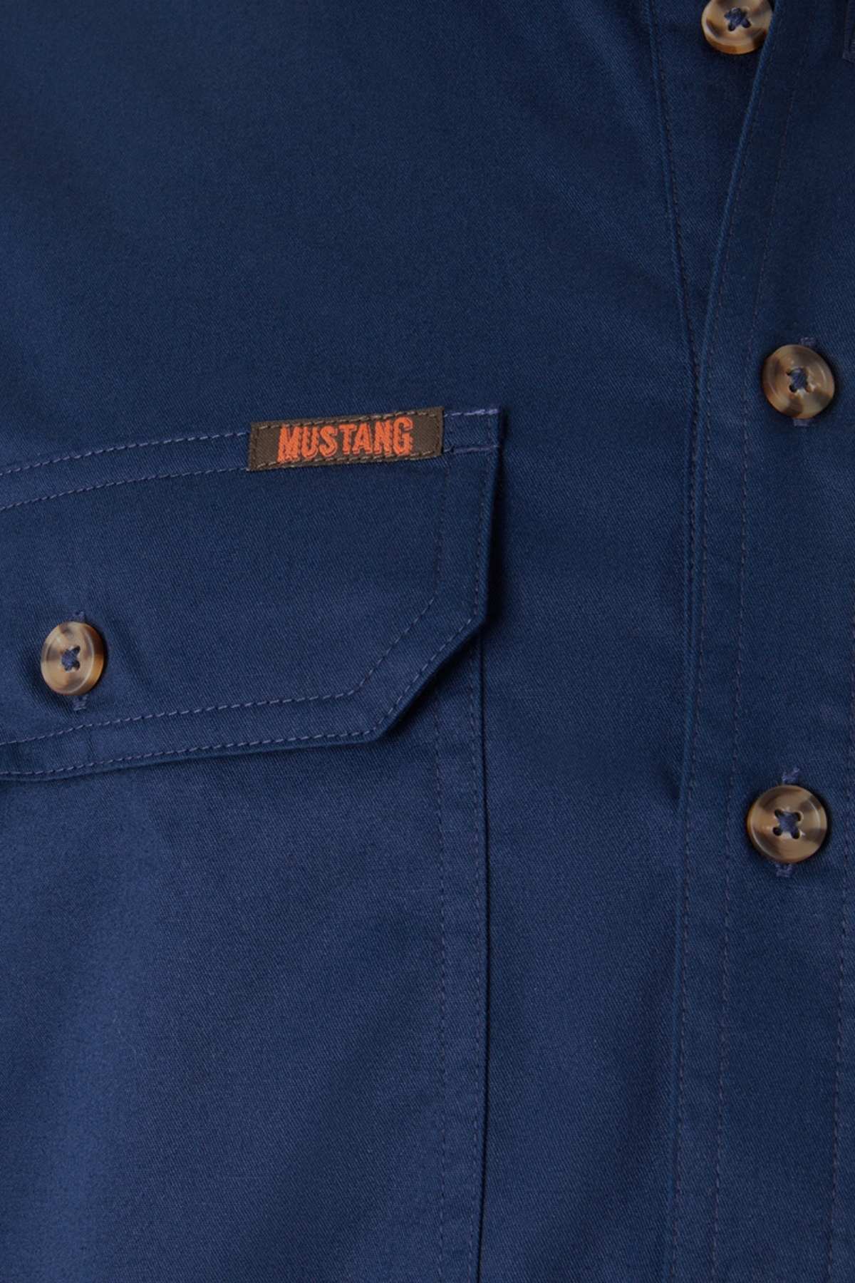 Close-up of the Mustang Signature Closed Front Workshirt in blue, featuring brown buttons, a chest pocket, durable cotton fabric, and an orange "MUSTANG" label above the pocket.