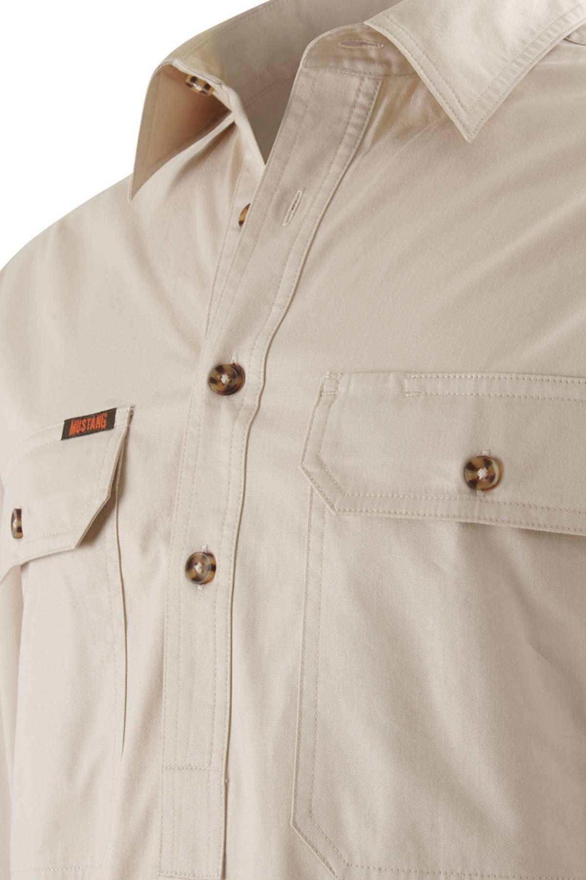 A close-up image of the cream-colored Mustang Signature Closed Front Workshirt for men highlights its chest pockets, brown buttons, and a small tag with text on the left pocket. The durable cotton fabric has a smooth texture, and it includes a classic collar.