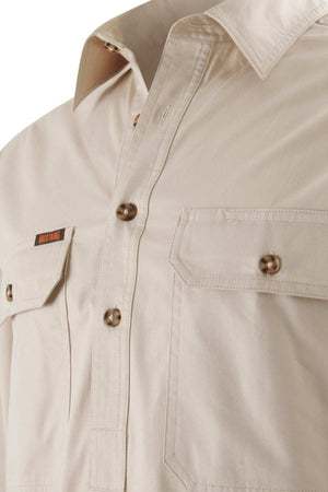 A close-up image of the cream-colored Mustang Signature Closed Front Workshirt for men highlights its chest pockets, brown buttons, and a small tag with text on the left pocket. The durable cotton fabric has a smooth texture, and it includes a classic collar.