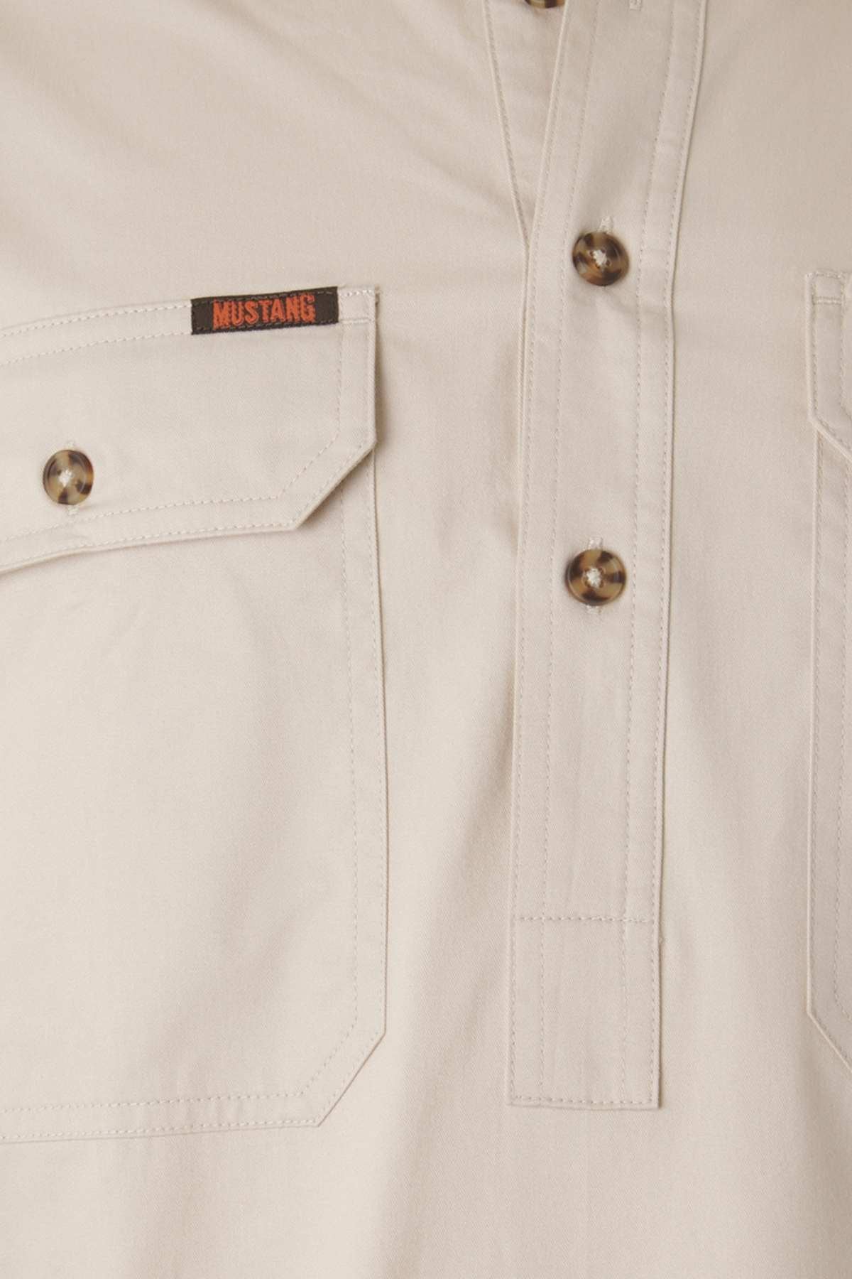 Close-up image of the Mustang Signature Closed Front Workshirt in beige, featuring a pocket with a button flap on the left chest. The pocket has a black and red "MUSTANG" label above it. This durable cotton workshirt includes a button placket with four brown buttons.