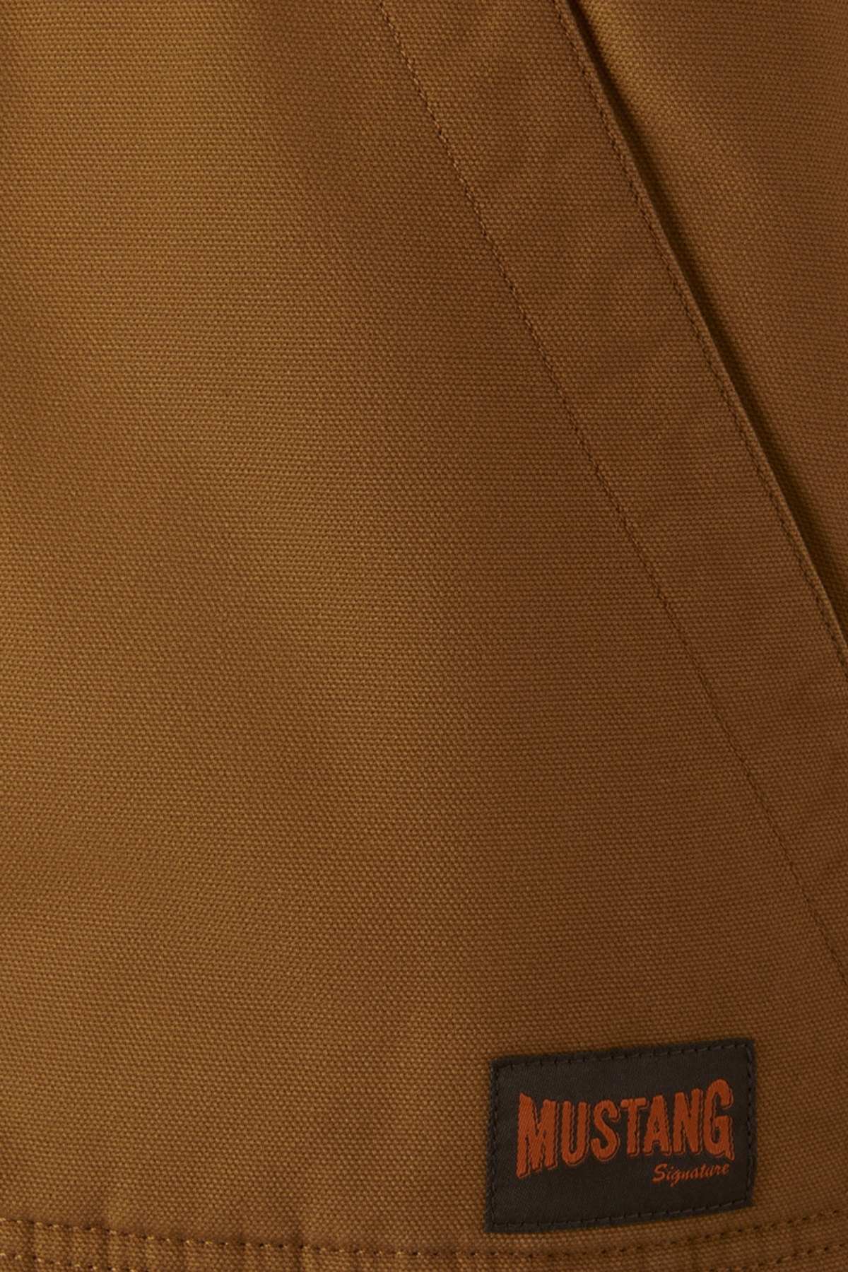 Close-up of the Mustang Signature Outback Canvas Vest, highlighting its durable canvas fabric, visible seam, and a black rectangular patch in the corner that says "MUSTANG Signature" in orange letters.
