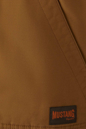 Close-up of the Mustang Signature Outback Canvas Vest, highlighting its durable canvas fabric, visible seam, and a black rectangular patch in the corner that says "MUSTANG Signature" in orange letters.