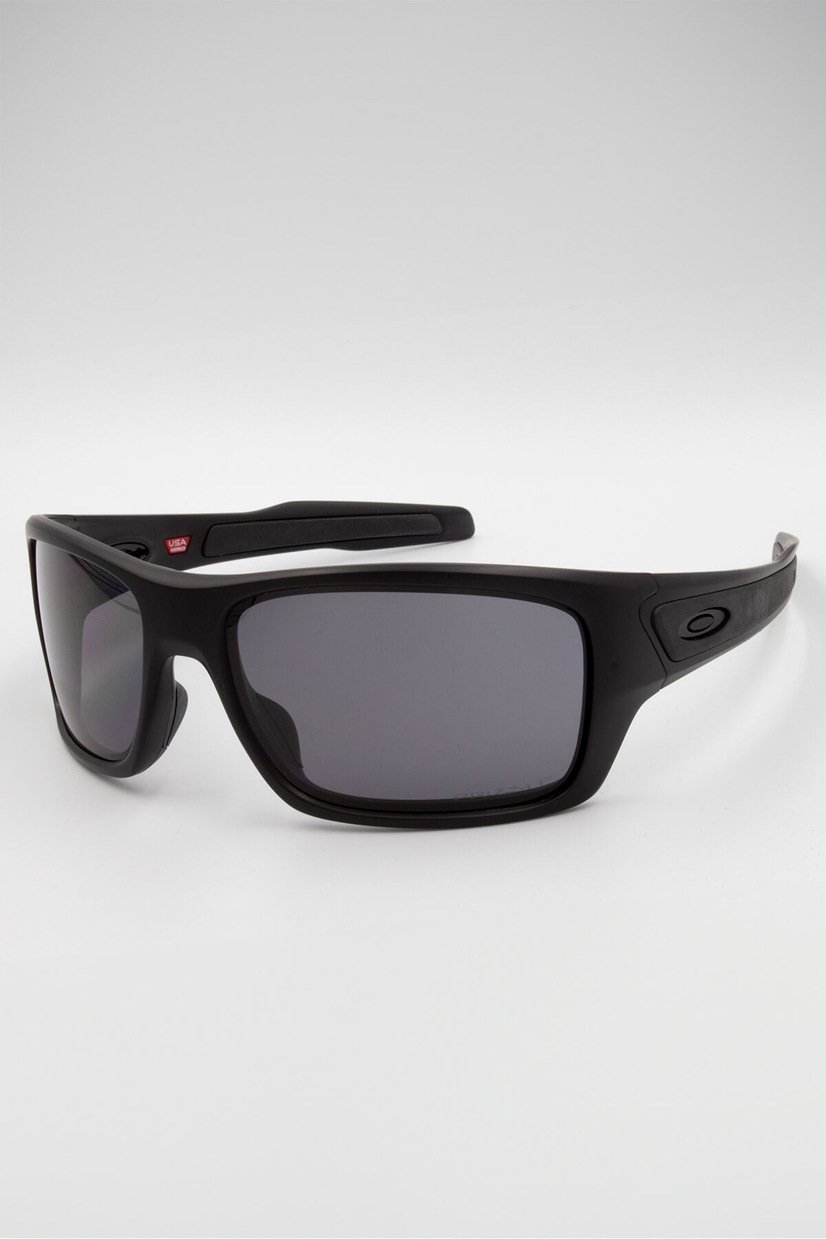 The Oakley Turbine sunglasses feature a modern design with matte carbon black rectangular frames, dark gray tinted lenses, and a subtle logo on the arms, displayed on a plain white background.