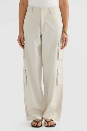 The person is wearing ORTC Arden Cargo Pants in a beige shade, featuring several cargo pockets. These pants are paired with a white top and black sandals. They stand in a neutral pose against a plain background, highlighting the seamless mix of tencel-cotton fabric in their outfit.