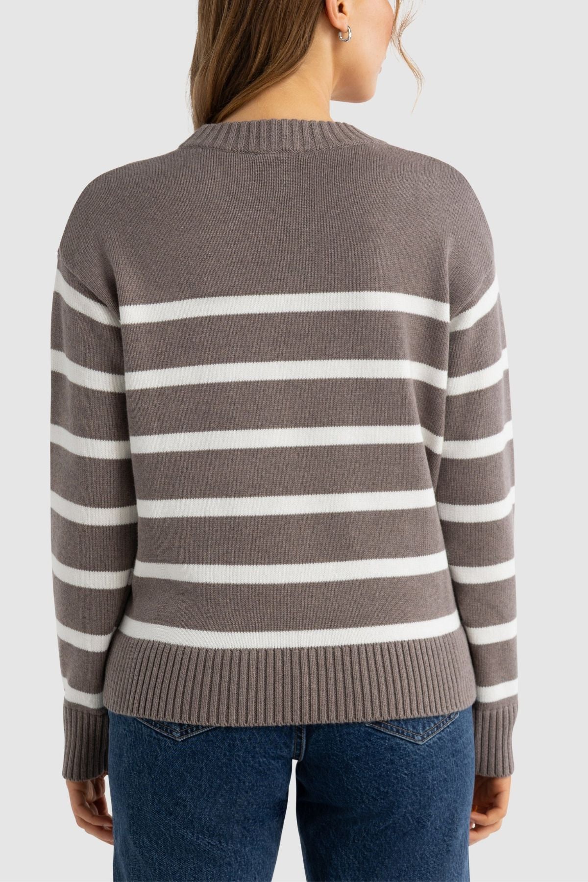 A person with light brown hair is shown from the back against a plain light background, wearing the ORTC Astrid Crew Knit—a relaxed fit sweater with white horizontal stripes—and blue jeans.