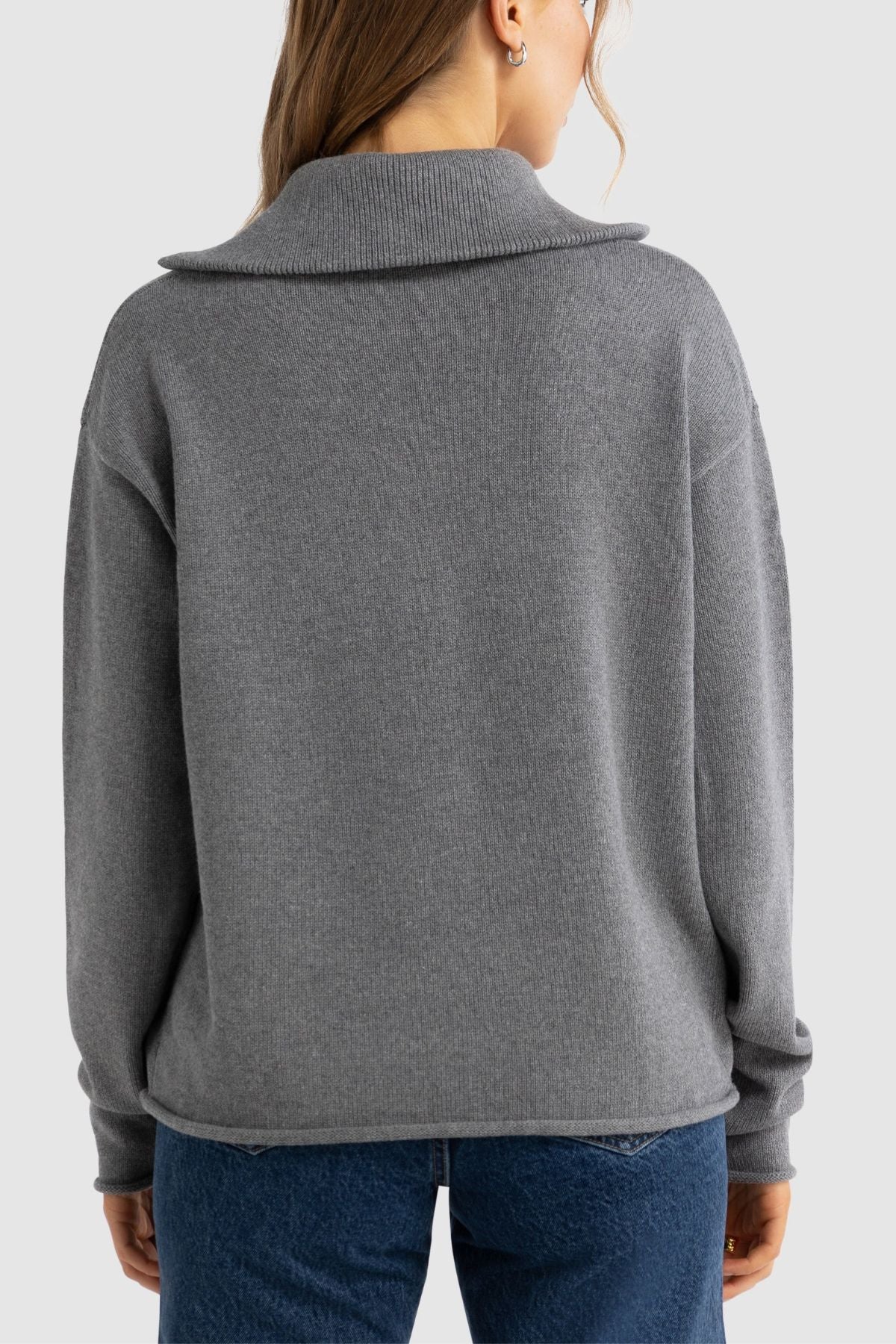 A person with long hair is shown from the back, wearing the ORTC Astrid Knit Quarter Zip sweater and blue jeans against a plain light background.