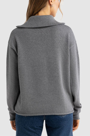 A person with long hair is shown from the back, wearing the ORTC Astrid Knit Quarter Zip sweater and blue jeans against a plain light background.