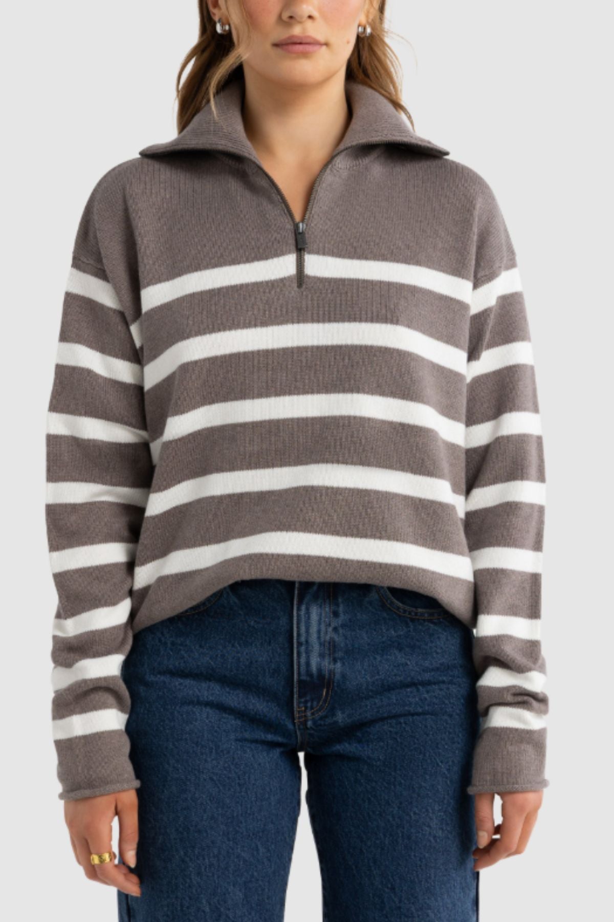 A woman wears the ORTC Astrid Knit Quarter Zip, a gray and white striped sweater with a collar, paired with blue jeans against a plain light background.
