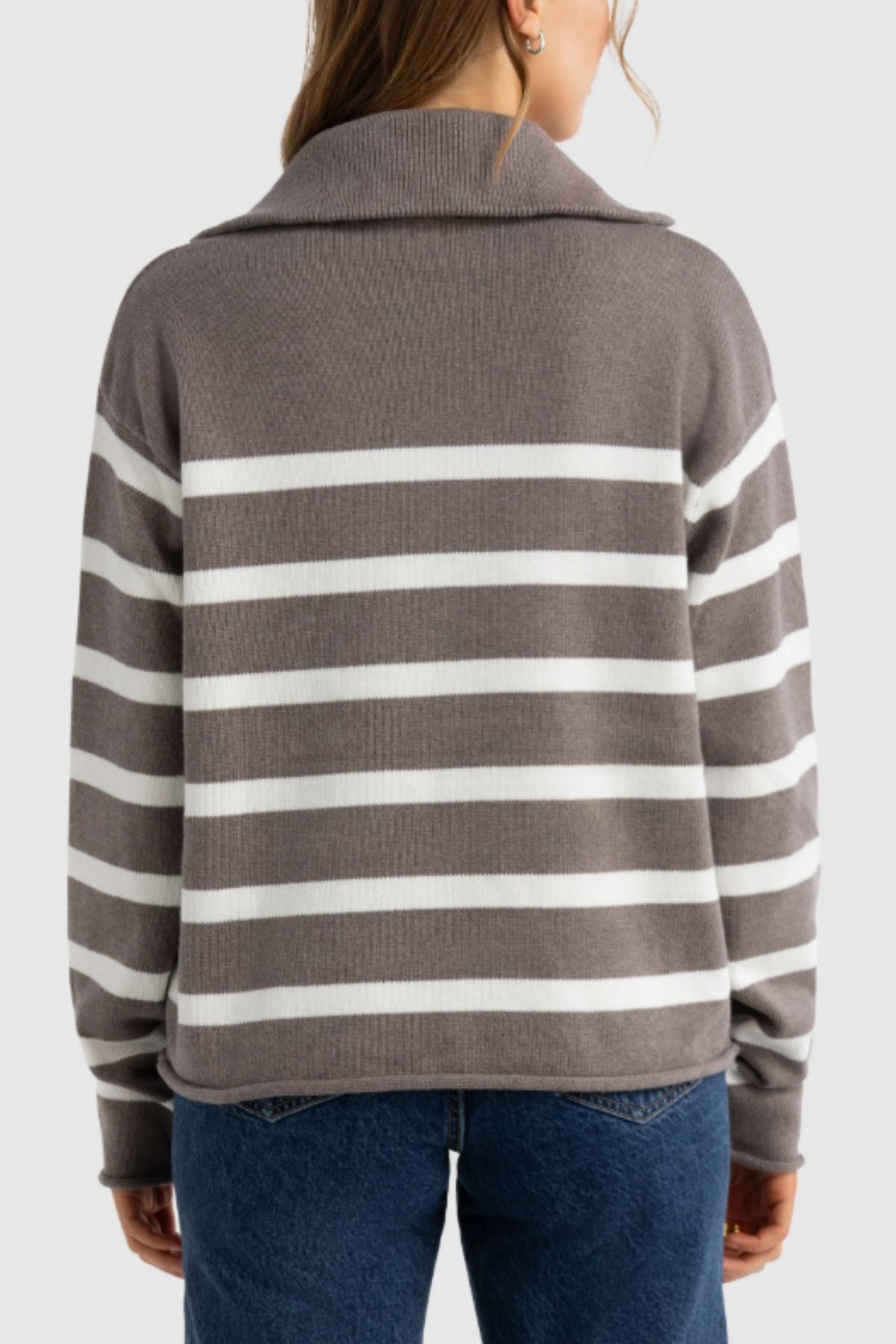 Seen from behind, a person with medium-length brown hair wears the ORTC Astrid Knit Quarter Zip—a gray sweater with white stripes—paired with blue jeans, standing out against a plain light background.