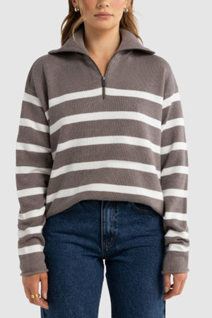 A woman wears the ORTC Astrid Knit Quarter Zip, a gray and white striped sweater with a collar, paired with blue jeans against a plain light background.