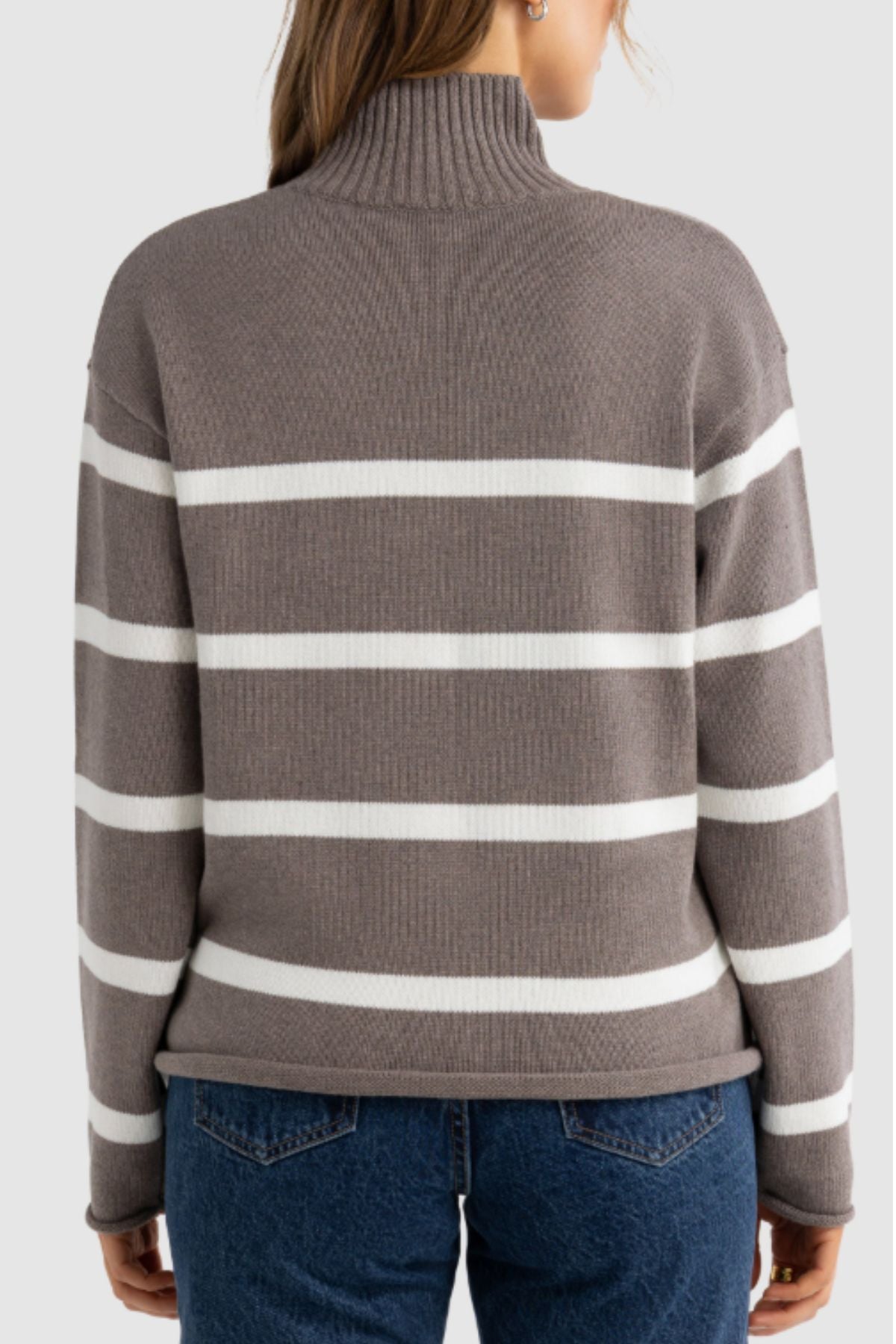 A person wearing the ORTC Astrid Knit Sweater, a taupe and white striped cotton-cashmere turtleneck, with blue jeans is shown from the back against a plain light gray background.