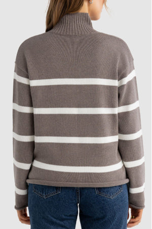 A person wearing the ORTC Astrid Knit Sweater, a taupe and white striped cotton-cashmere turtleneck, with blue jeans is shown from the back against a plain light gray background.