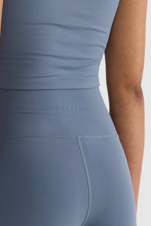 A person in blue athletic wear, featuring ORTC Eva 6 Inch Bike Shorts made from recycled polyester. The ensemble includes a sleeveless top and high-waisted leggings, ideal for sports activities. The material is smooth and stretchy, with the brand name subtly embossed on the waistband.