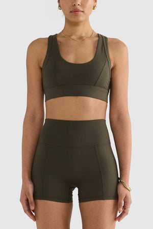 A person wearing the ORTC Eva Crop Top in olive green with matching high-waisted shorts, both crafted from recycled polyester, stands against a plain white background. They accessorize with a necklace and bracelet, completing the look with style and eco-consciousness.