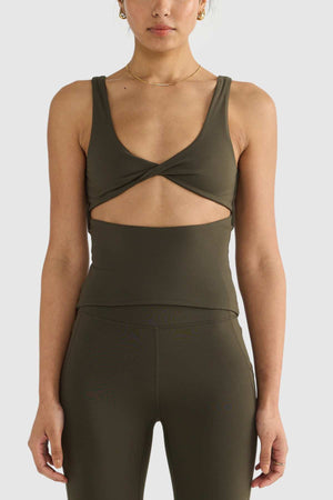 The woman is wearing an ORTC Eva Twist Back Reversible Top in dark green, highlighting its versatile dual-wear design with a twist front cutout. She completes her look with matching high-waisted leggings, both crafted from ultra-soft double-brushed fabric for maximum comfort.