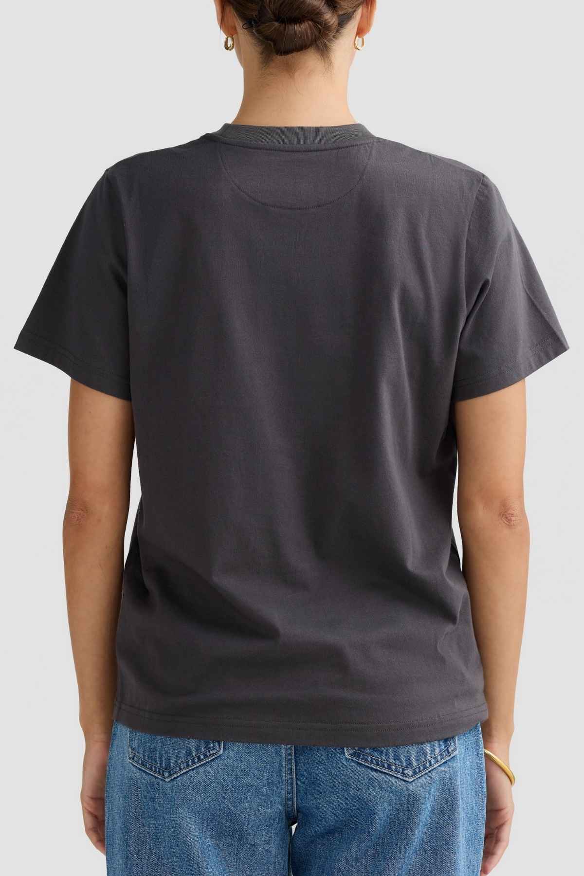 A person with braided hair is wearing a relaxed-fit ORTC Everyday T-Shirt in plain dark grey paired with blue jeans, showcased from behind against a light grey background. The soft mid-weight cotton fabric enhances the casual elegance of the outfit.