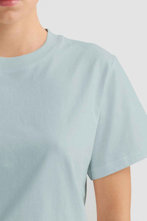 A person dressed in a light blue ORTC Everyday T-Shirt is partially visible, with an emphasis on the upper torso, showcasing the T-shirt's comfort and style against a simple backdrop.