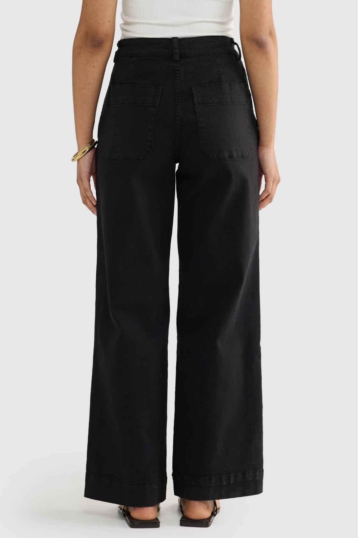 Someone wearing the ORTC Lottie Relaxed Twill Pants is standing with their back facing the camera, highlighting a high-waisted, wide-leg relaxed fit. They have paired it with a white top and black sandals, and are accessorizing with a bracelet on their right wrist.