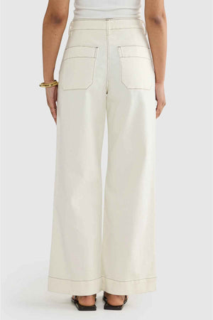 A person is shown from the back wearing ORTC Lottie Relaxed Twill Pants, which are wide-leg and high-waisted, with a sleeveless top. These stretch cotton twill pants, designed in Australia, feature large back pockets. The outfit is accessorized with gold bangles and paired with black sandals.