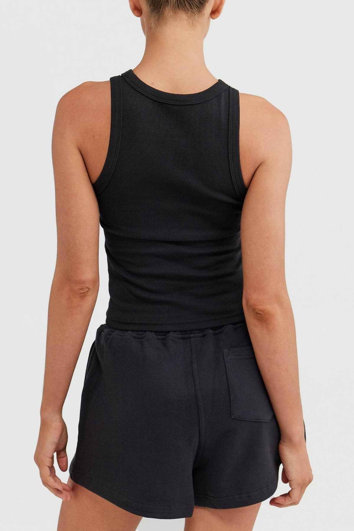 An individual is dressed in a ribbed knit ORTC Mimi Rib Tank and dark shorts, facing away.