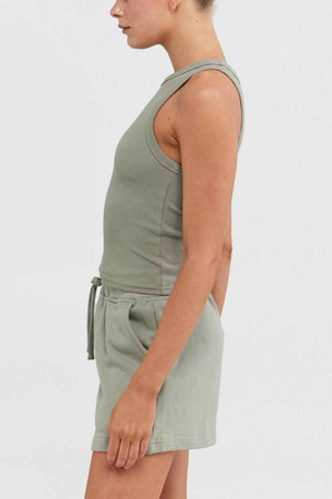 A person sporting an ORTC Mimi Rib Tank—a sleeveless green top complemented by matching drawstring shorts, both crafted from ribbed knit fabric—stands in profile against a plain white background.