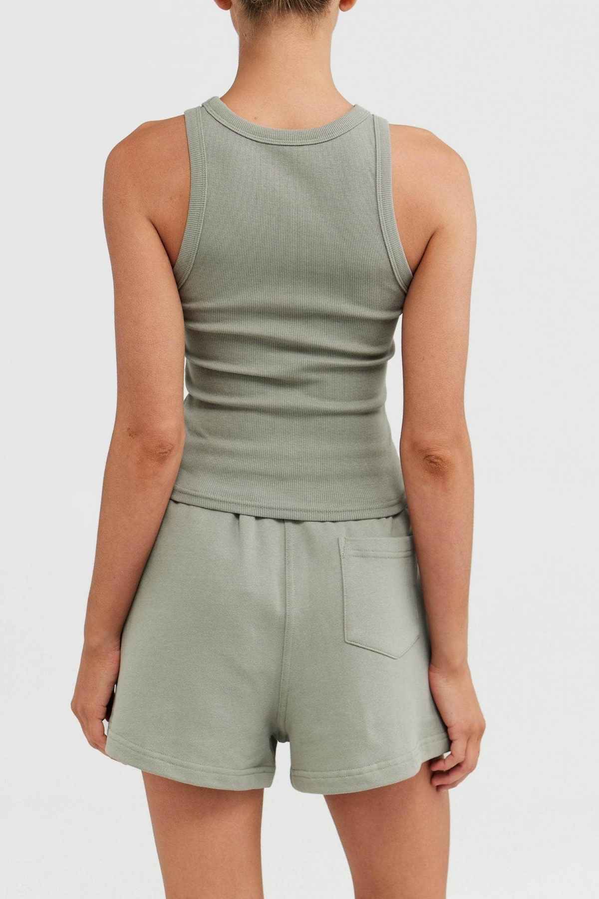 Rear view of an individual dressed in the ORTC Mimi Rib Tank in a light green ribbed knit fabric, coupled with coordinating shorts that include a back pocket, set against a simple white backdrop.