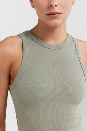 A person wearing the ORTC Mimi Rib Tank, made from ribbed knit fabric, poses against a plain background. The image highlights their upper body and clothing, showcasing a neutral expression, making it an ideal layering addition to any wardrobe.