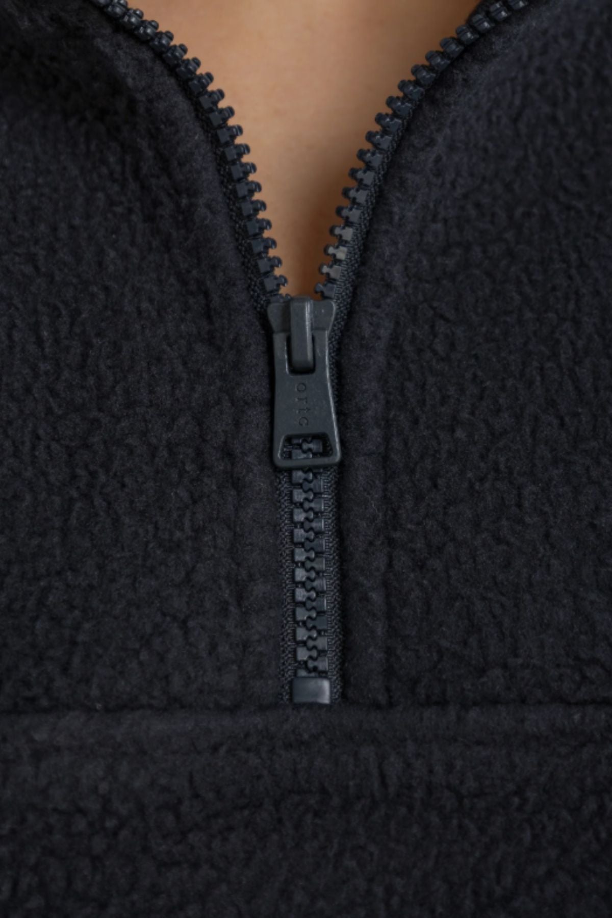 Close-up of the ORTC Sherpa Fleece Quarter Zip in black, made from recycled polyester, with a partially unzipped quarter zip that reveals its textured fabric and a hint of skin at the top.