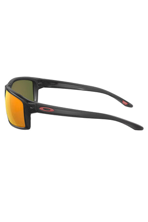 Side view of Oakley Gibston Polarized sunglasses with black frames, orange-yellow reflective Prizm lenses, and a red Oakley logo on the temples, featuring advanced Polarised Prizm lens technology.