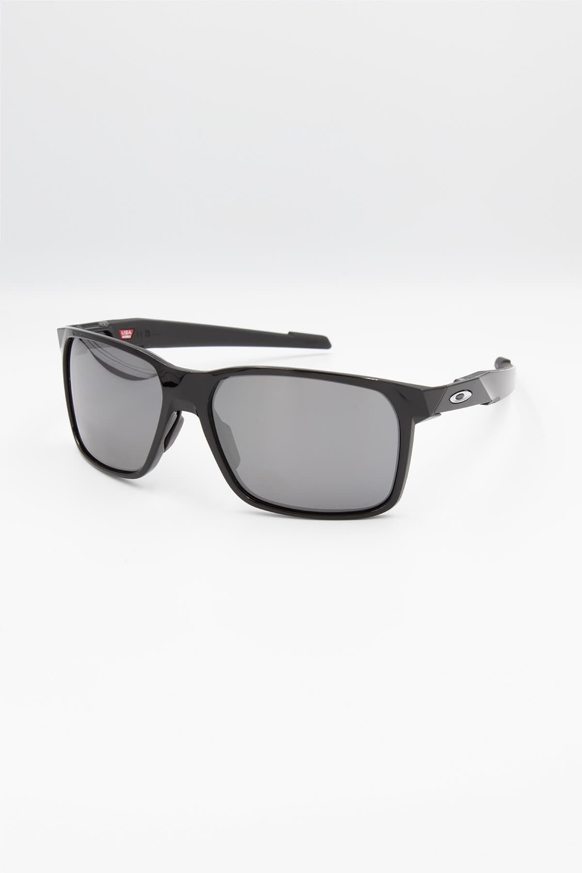 On a white background, the Oakley Portal X Polarized sunglasses showcase black rectangular frames with dark lenses. The sleek arms feature a small logo, epitomizing Oakley's stylish design.