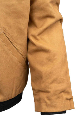 Close-up of a person wearing the Outback Canvas Sawbuck Hoodie, featuring a tan color, side pocket, and black cuff detail in water-resistant fabric. Only the arm and torso appear against a plain white background.