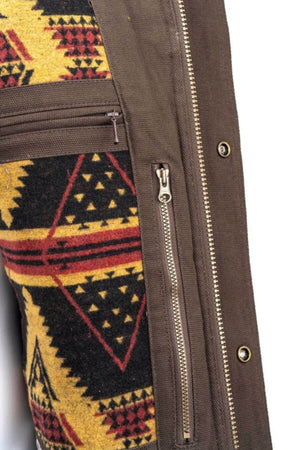 Close-up of the Outback Cattleman Jacket showcasing a brown vertical zipper on brown fabric next to a patterned section with black, red, and yellow geometric shapes. The patterned area features a horizontal zipper. The jacket also includes multiple pockets for all your essentials.