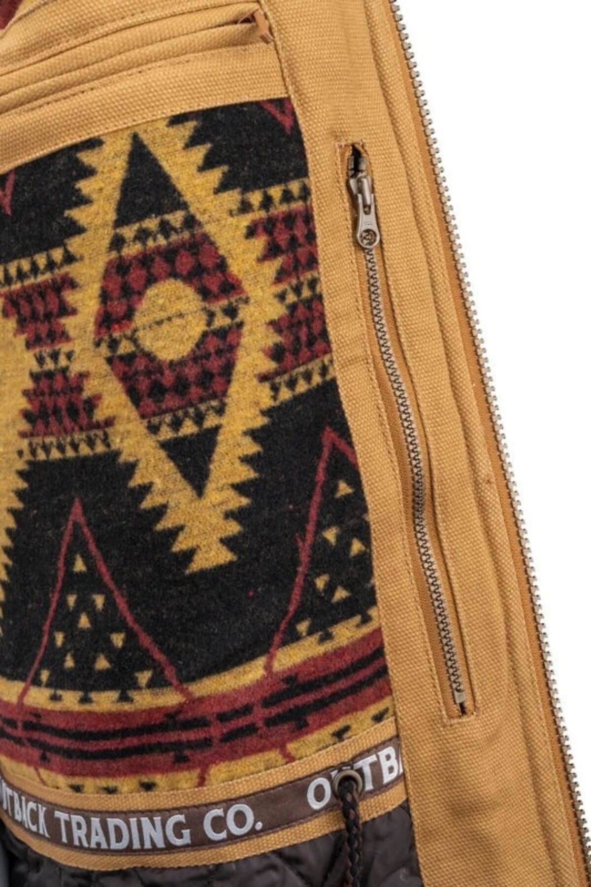 A close-up of the Outback Cattleman Jacket shows a fabric panel with a geometric, tribal-inspired design in red, yellow, and black. It's framed by mustard-colored fabric with a zippered pocket and features a waistband branded "OUTBACK TRADING CO." Perfect for outdoor adventures.