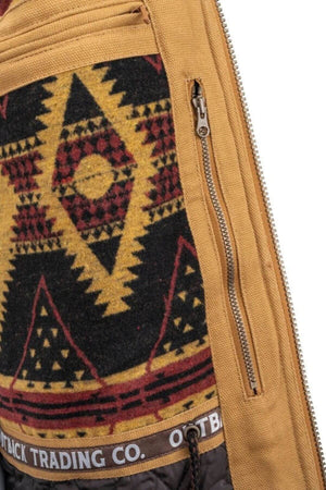 A close-up of the Outback Cattleman Jacket shows a fabric panel with a geometric, tribal-inspired design in red, yellow, and black. It's framed by mustard-colored fabric with a zippered pocket and features a waistband branded "OUTBACK TRADING CO." Perfect for outdoor adventures.