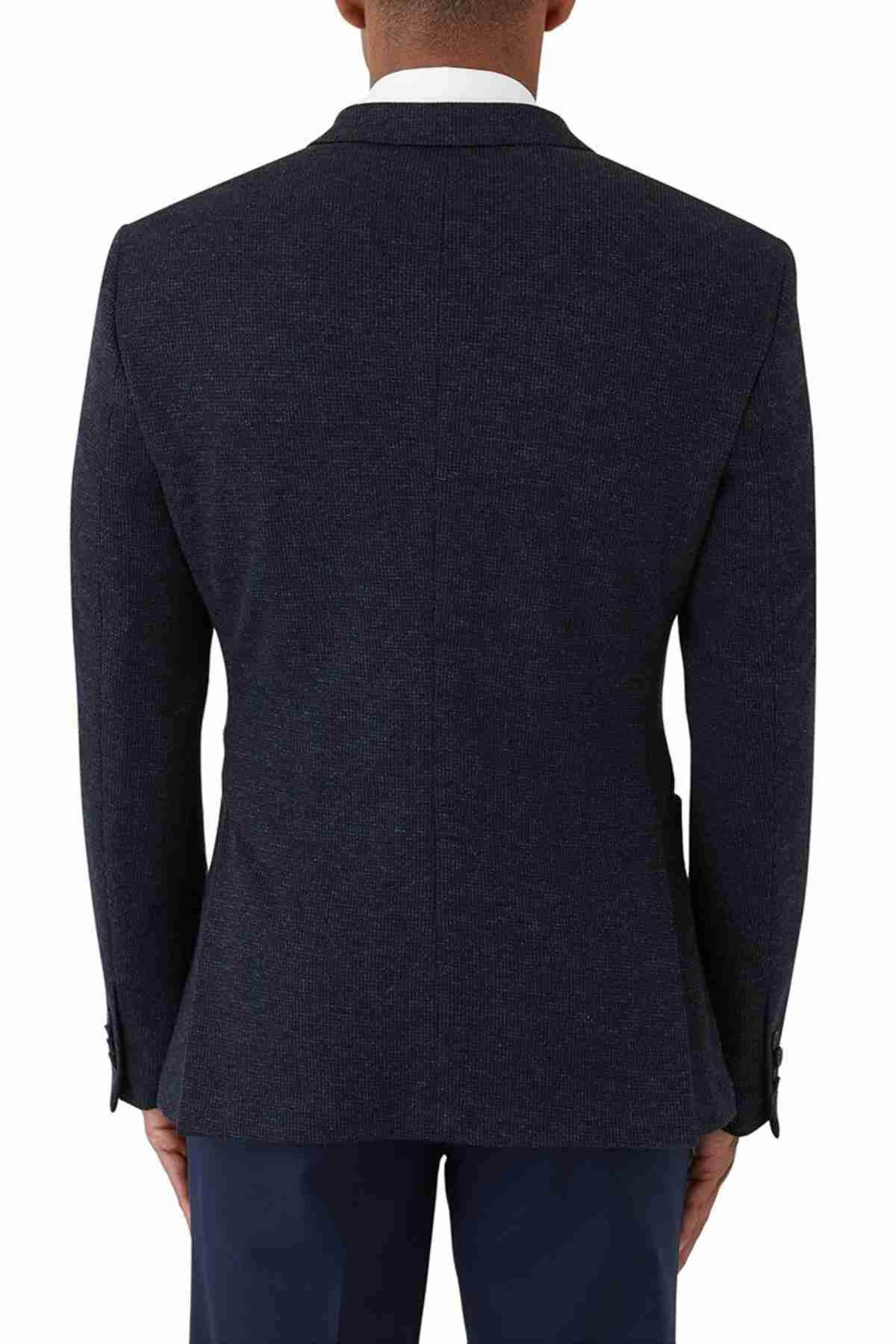 A person is seen from the back wearing an Uberstone Zeller Jacket, a navy skinny-fit blazer with notch lapels and button detailing on the sleeves, paired with a white shirt and dark pants against a plain white background.