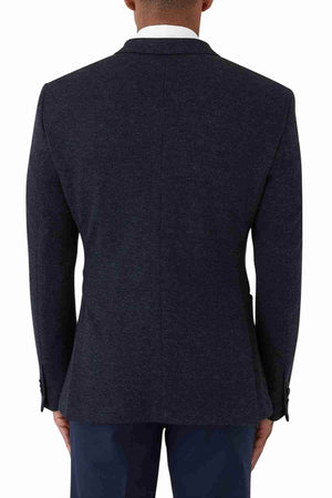 A person is seen from the back wearing an Uberstone Zeller Jacket, a navy skinny-fit blazer with notch lapels and button detailing on the sleeves, paired with a white shirt and dark pants against a plain white background.