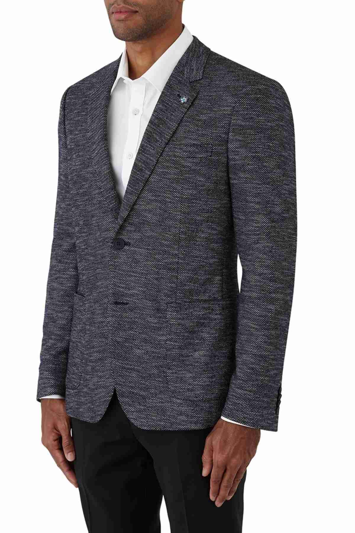 A man models the Uberstone Zeller Jacket, a textured dark skinny fit style, over a white dress shirt and black trousers. He stands with hands at his sides, turned slightly left against a plain white background.
