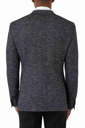 A man is seen from behind wearing the Uberstone Zeller Jacket, a dark gray wool blend blazer with a subtle pattern, tailored for a refined fit. He pairs it with a white dress shirt and black pants.