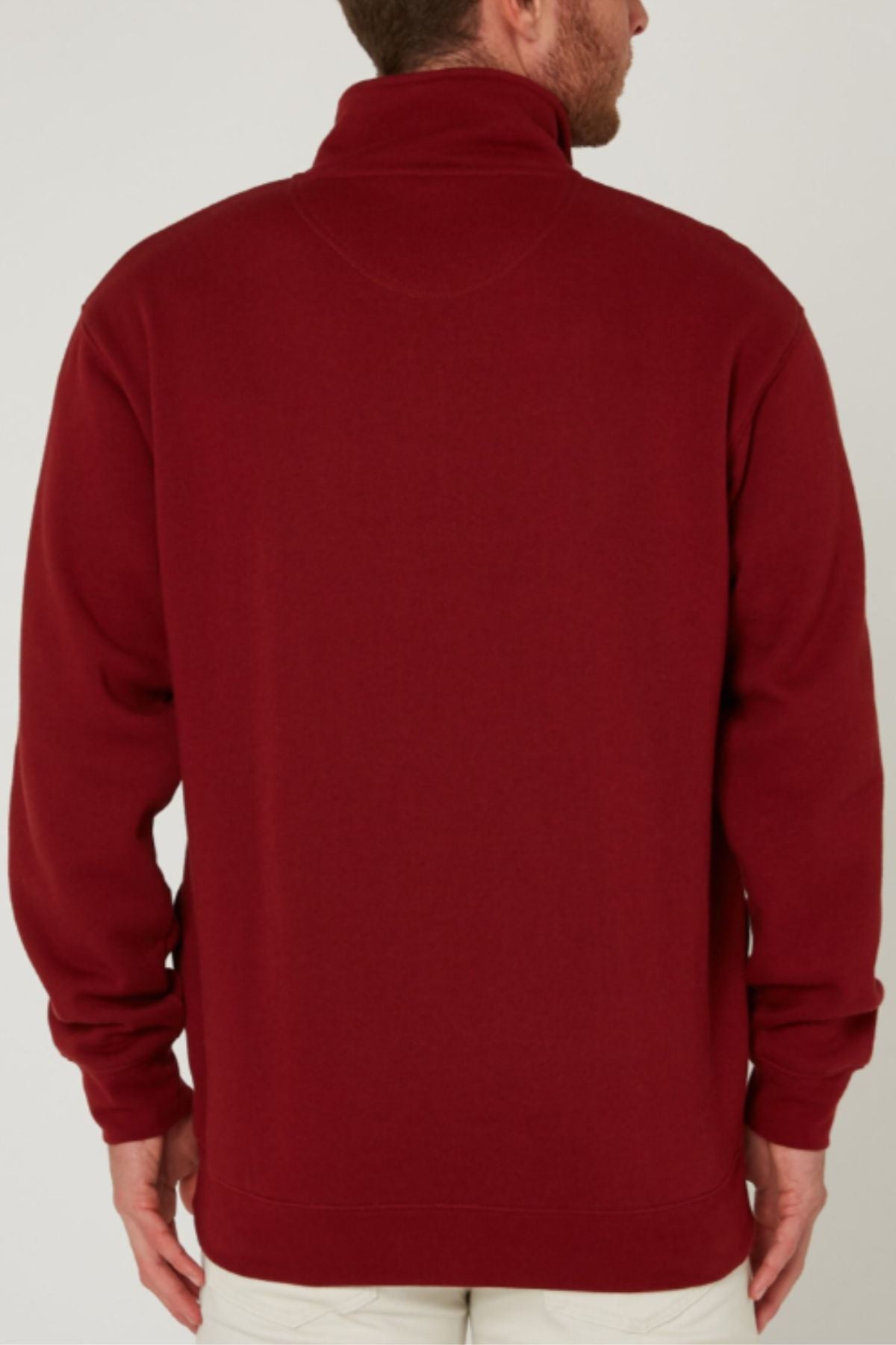 A man is seen from behind wearing the Pilbara Classic Fleece Pullover, a high-collared, maroon top with long sleeves and a fleece lining. His short hair and light-colored pants stand out against the plain background, highlighting his cozy look.