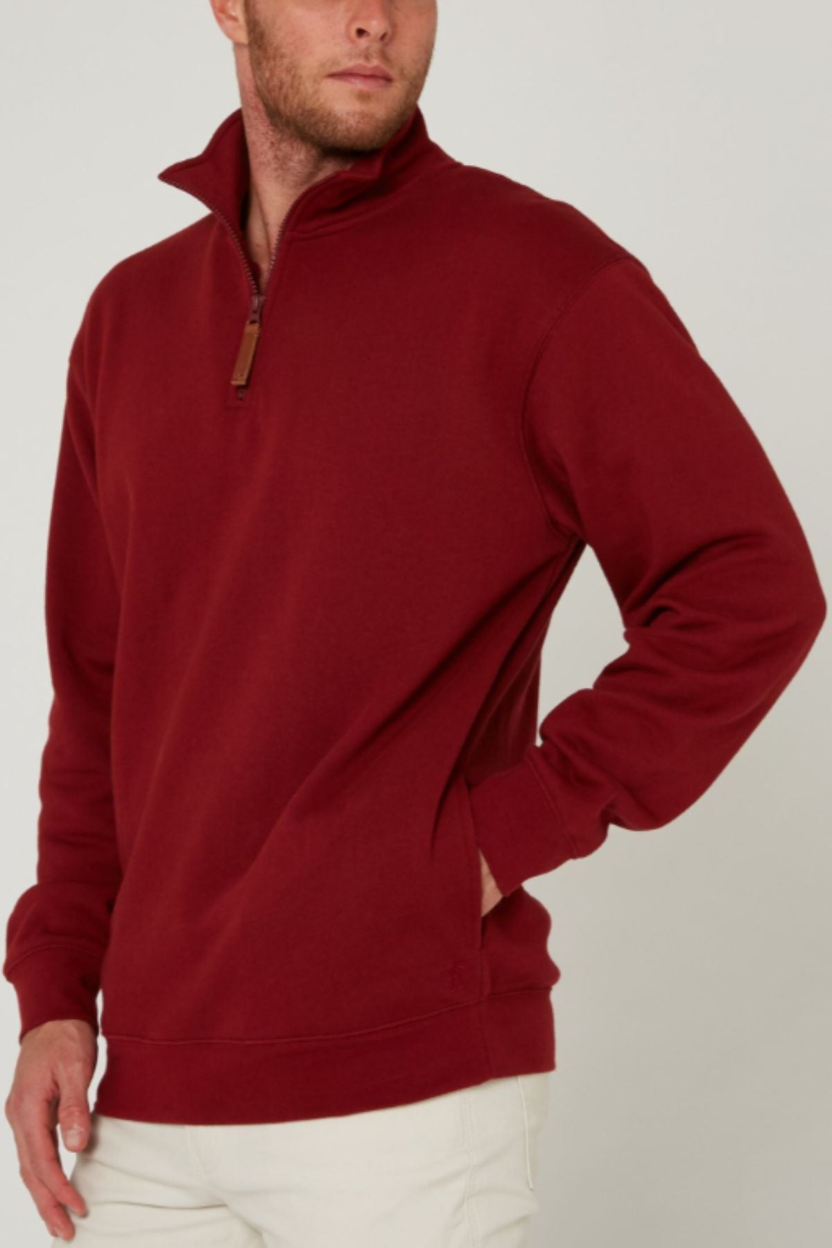 A person wearing a maroon Pilbara Classic Fleece Pullover with a stand-up collar and white pants poses with one hand in their pocket against a neutral background.