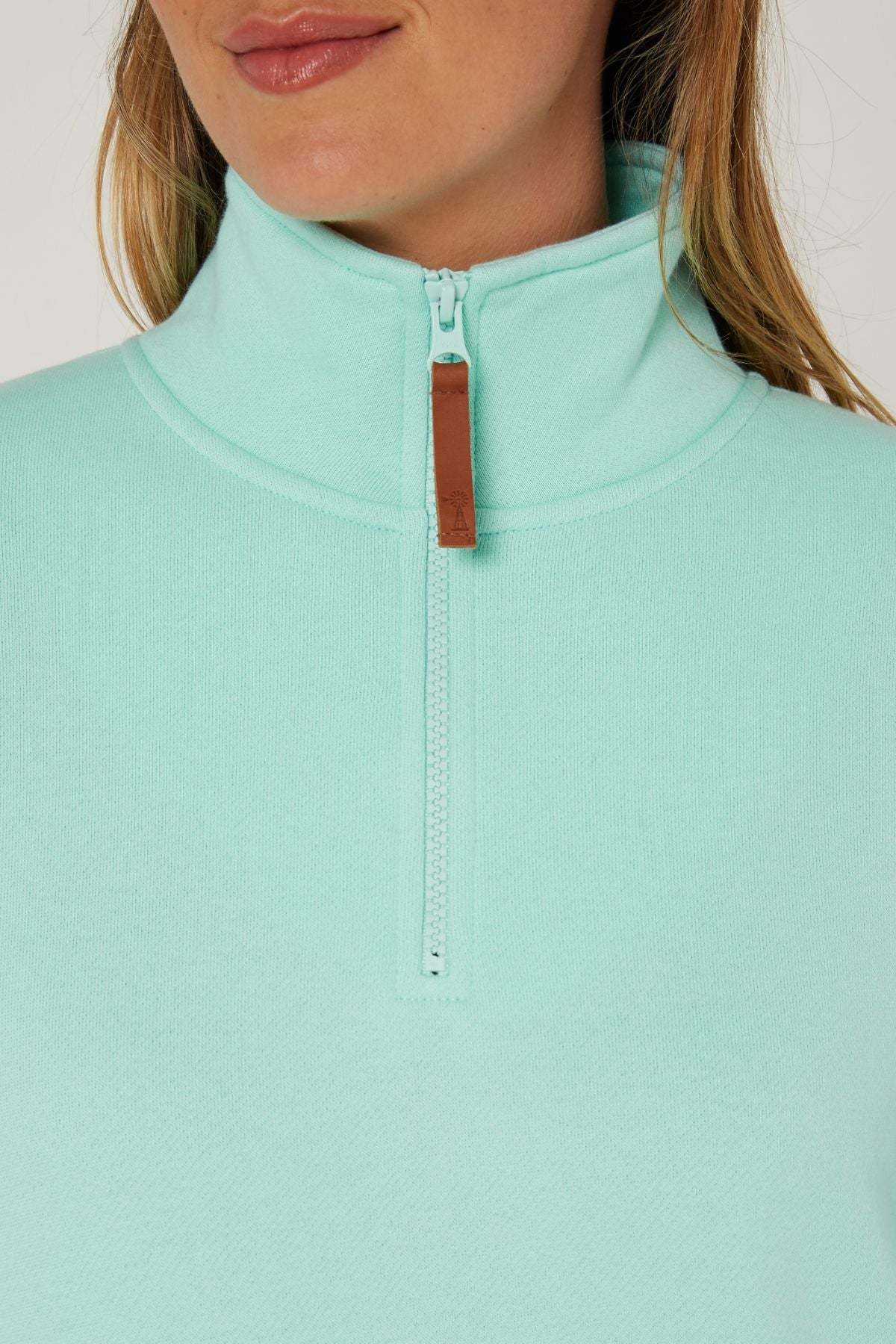 A close-up of a person wearing a light turquoise Pilbara Ladies Classic Fleece Pullover with a brown zipper pull. Only the lower face and upper torso are shown, hinting at the pullover’s soft fleece lining.