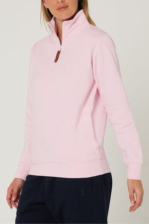 A person wearing a light pink Pilbara Ladies Classic Fleece Pullover with a high collar and cozy fleece lining, paired with navy blue pants, stands against a plain, light-colored background.