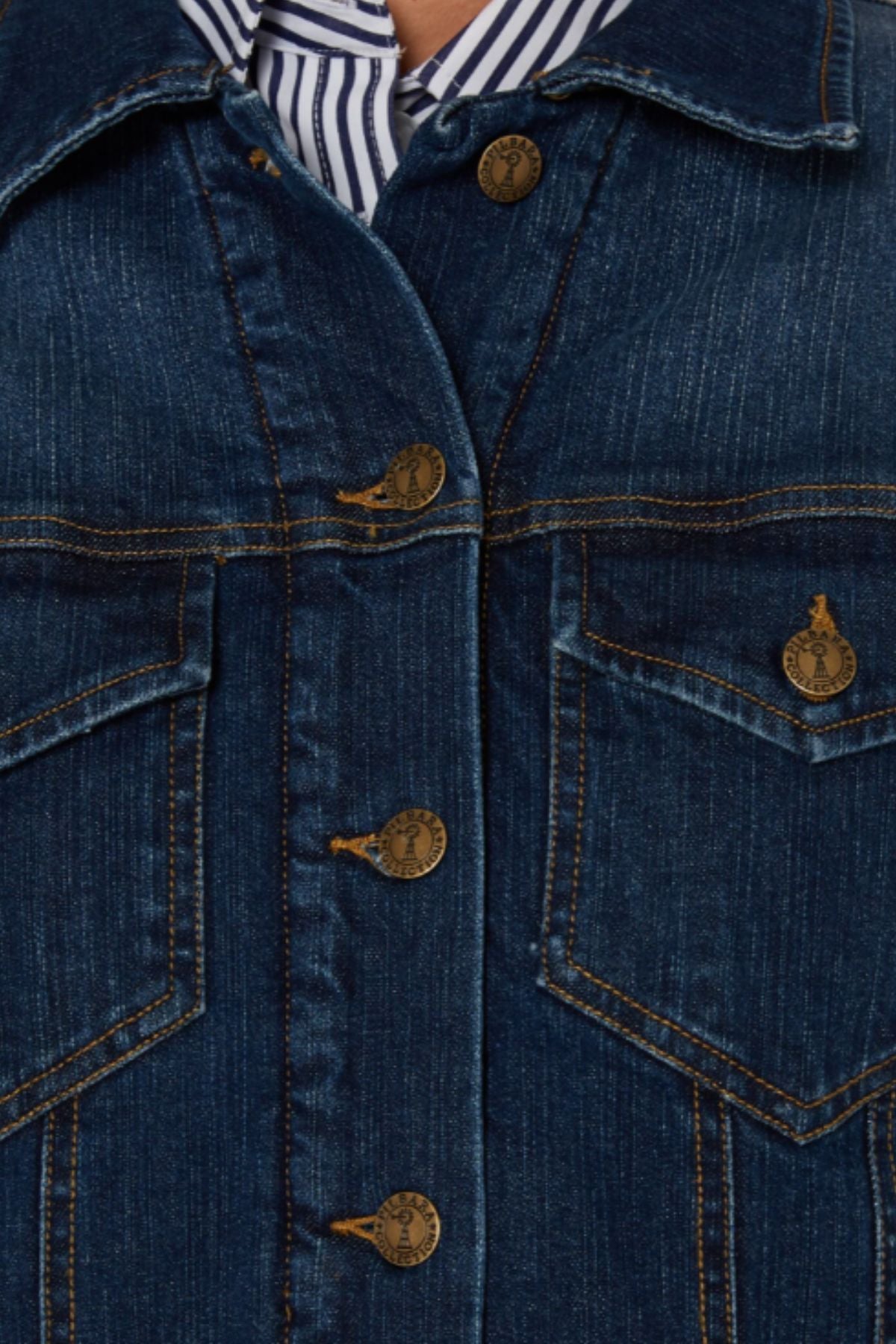 Close-up of a blue Pilbara Lauren Sherpa Lined Jacket with bronze buttons and yellow stitching, featuring two chest pockets with flaps, worn over a blue and white striped shirt.