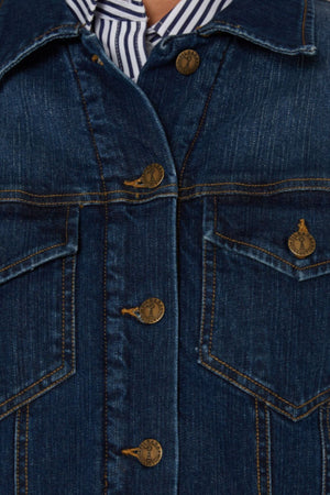 Close-up of a blue Pilbara Lauren Sherpa Lined Jacket with bronze buttons and yellow stitching, featuring two chest pockets with flaps, worn over a blue and white striped shirt.