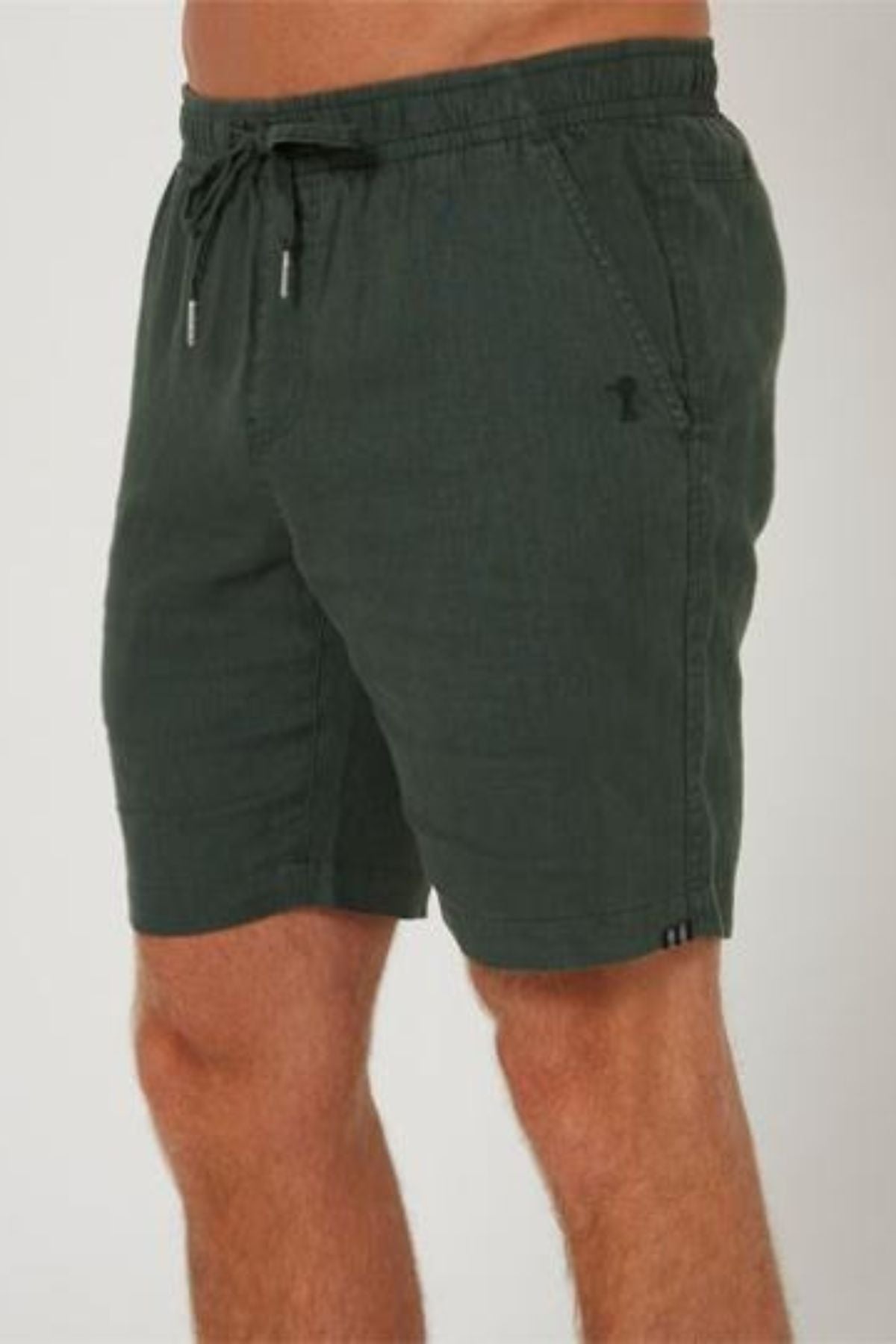 A person wearing Pilbara Linen Short in dark green with side pockets, standing against a plain light background.